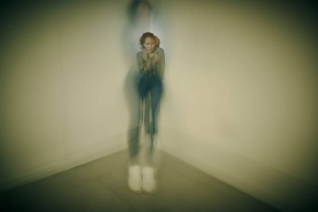 A blurred image shows a woman standing in a corner, hugging herself. This image relates to the topic of Emotional Distress and Reputational Harm Awards.